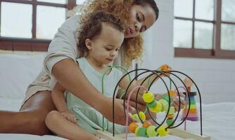 Happy mother and daughter playing with a toy developing colorful wooden blocks on bed together at home. photo