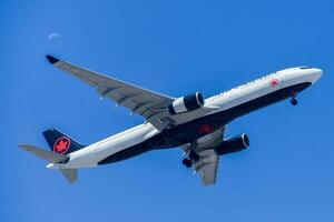 Canadian air company Air Canada with aircraft Airbus A330-300 approaching to land at Lisbon International Airport against blue sky photo