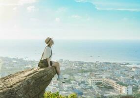 image of a girl sitting on a mountain looking down at the sea photo