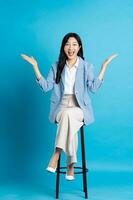 Asian businesswoman portrait sitting on chair, isolated on blue background photo