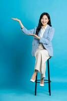 Asian businesswoman portrait sitting on chair, isolated on blue background photo