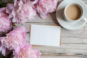 simula una tarjeta de papel blanco en blanco para texto y delicadas peonías sobre un fondo de madera. endecha plana, vista superior. lugar para el texto. tarjeta de felicitación foto