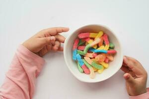 child hand pick colorful candy sweet jelly in a bowl on table photo