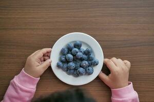 top view of child hand pick fresh blueberries in a bowl photo