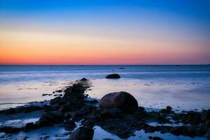 Sunset, stone beach with small and large rocks in front of the illuminated sea. photo