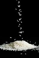 Raw white rice is falling on table. Pile of uncooked long rice on black background. photo