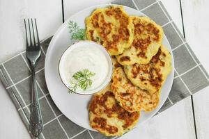 Zucchini pancakes with cream sauce on plate. Healthy diet food. Dinner table setting. photo