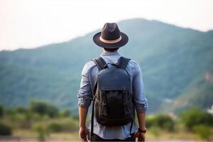 Back view of young man with backpack and hat standing on top of the mountain photo