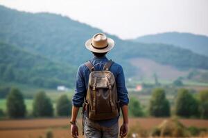 Back view of young man with backpack and hat standing on top of the mountain photo