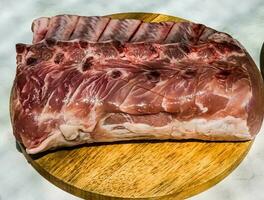 Fresh whole raw pork steak with ribs on a wooden kitchen board. Big piece of pig meat close up photo