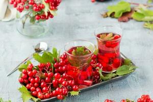 A decoction of ripe viburnum berries in glasses and branches with berries and leaves of viburnum on a substrate on the table. Alternative medicine, wellness and vitamin nutrition photo