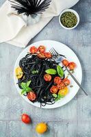 Appetizing black spaghetti with dried tomatoes, pumpkin seeds and sesame seeds on a white plate on the table. Gourmet food. Top and vertical view photo