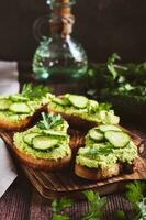 Appetizing toasts with guacamole, cucumbers and herbs on a wooden board vertical view photo