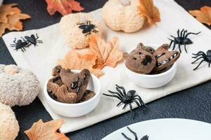 A delicious Halloween treat - gingerbread cookies with chocolate icing in bowls on a table with pumpkins and leaves. Traditional celebration, sweet food. photo