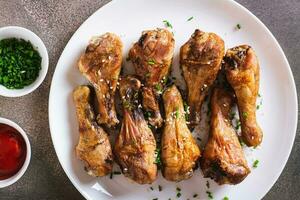 Closeup of baked chicken drumsticks with green onions and sesame seeds on a plate top view photo