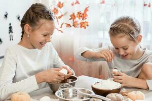 Two cute girls put eggs and flour into gingerbread dough for baking halloween cookies at home kitchen. Treats and preparations for the halloween celebration photo