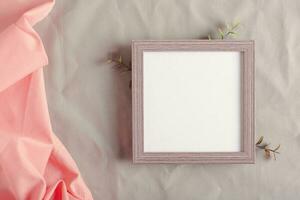 Mockup empty photo frame and branches on green cotton fabric top view