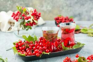 Infusion of viburnum berries in glasses and twigs with berries and viburnum leaves on a substrate on the table. Alternative medicine, wellness and vitamin nutrition photo