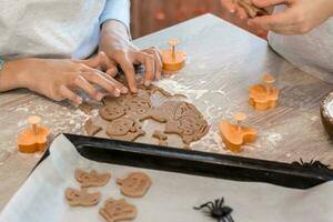 Preparing to celebrate halloween and preparing a treat. Children cut out baking pans for Halloween cookies and a baking sheet of raw cookies on the table. Lifestyle photo