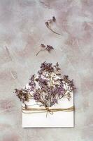 A bouquet of dried flowers in a light envelope tied with a rope on a textured background. Greeting romantic card. Top and vertical view photo