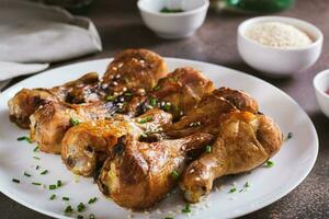 Spicy baked chicken drumsticks with green onions and sesame seeds on a plate photo