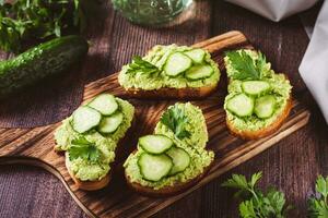 Crostini with avocado puree, cucumbers and herbs on a wooden board photo