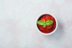 Tomato paste and basil leaves in a bowl on a light background. Vegetable and vegetarian food. Vitamins and detox diet. Copy space. Top view photo