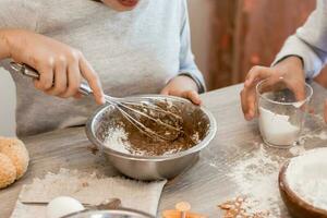 Preparing to celebrate halloween and preparing a treat. Children whisk gingerbread dough with a whisk in a baking bowl for Halloween cookies at home in the kitchen. Lifestyle photo