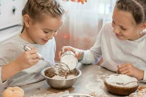 Preparing to celebrate halloween and preparing a treat. Two girls add wheat flour to baking cookie dough for Halloween at home in the kitchen. Lifestyle photo