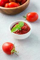 Tomato paste and basil leaves in a bowl and a couple of fresh tomatoes on a light background. Vitamins and detox diet. Vegetable and vegetarian food. Vertical view photo