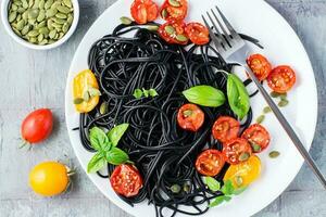 Black spaghetti with cuttlefish ink, with dried tomatoes, pumpkin seeds and sesame seeds on a plate on the table. Gourmet food. Top view. Close-up photo