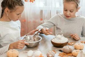 Two cute girls whip gingerbread dough to make halloween cookies in home kitchen. Treats and preparations for the halloween celebration photo