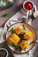 A la parrilla maíz con especias, mantequilla y ajo en un plato en el mesa parte superior y vertical ver foto