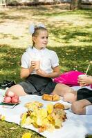 Chica de escuela niña en un picnic participación un eco taza con un Paja en un soleado otoño parque. al aire libre educación para niños. espalda a colegio concepto foto