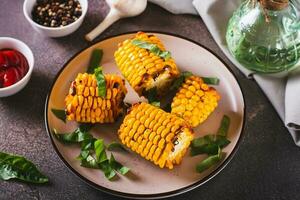 Grilled corn with spices, butter and garlic on a plate on the table photo
