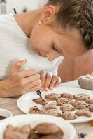 Preparing to celebrate halloween and preparing a treat. A girl paints halloween cookies on a plate with chocolate icing. Lifestyle photo