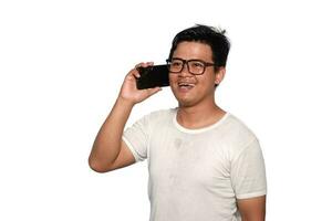 Excited Asian man with glasses wearing white Tshirt smiling while holding his phone, isolated by white background photo
