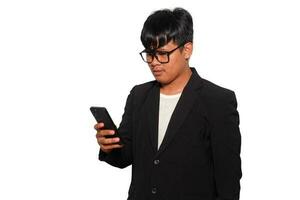 Excited Asian man with glasses wearing black suit smiling while holding his phone, isolated by white background photo