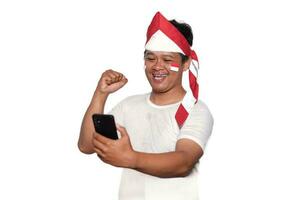 emocionado asiático hombre vistiendo blanco camiseta sonriente mientras participación su teléfono, aislado por blanco antecedentes. indonesio independencia día celebracion foto