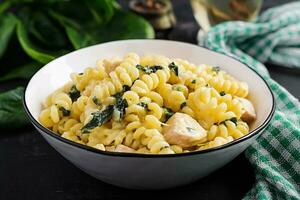 Fusilli pasta with a creamy sauce with chicken meat, parmesan cheese and spinach on a bowl on a dark background. photo