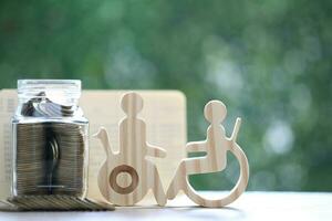 Man on wheelchair and gold coin money in the glass bottle on natural green background,Save money for prepare in future and handicapped person concept photo