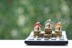 Finance, Model house on calculator and stack of coins money on natural green background,Business investment and real estate concept photo