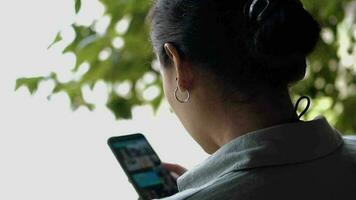 un asiatique femme est en jouant sa mobile téléphone dans sa mains tandis que séance sur une parc banc video