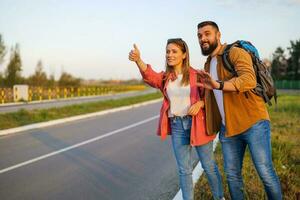 Happy couple hitchhiking on roadside trying to stop car. photo
