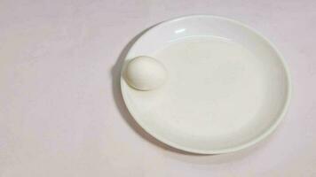 Stop motion animation of an egg moving on a white background and breaking on a white plate. video