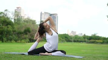 asiático atractivo joven mujer tener un hermosa cuerpo, jugando yoga en un elegante postura, en el verde parque, concepto a personas recreación y salud cuidado concepto. video