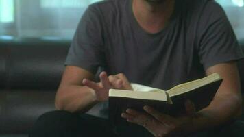 close-up young asian man reading a book or novel while relaxing on a sofa in his minimal living room. video