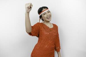 A young Asian woman with a happy successful expression wearing red kebaya and headband isolated by white background. Indonesia's independence day concept. photo