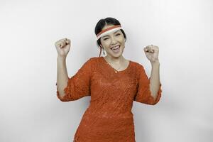 A young Asian woman with a happy successful expression wearing red kebaya and headband isolated by white background. Indonesia's independence day concept. photo