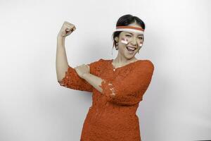 emocionado asiático mujer vistiendo un rojo kebaya y venda demostración fuerte gesto por levantamiento su brazos y músculos sonriente con orgullo de indonesia independencia día concepto. foto